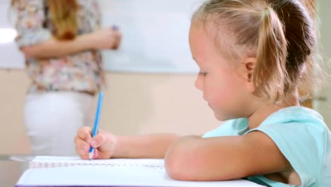 Kleine-süße-Mädchen-sitzt-im-Klassenzimmer-und-Studien-mit-Lehrer-im-Heft