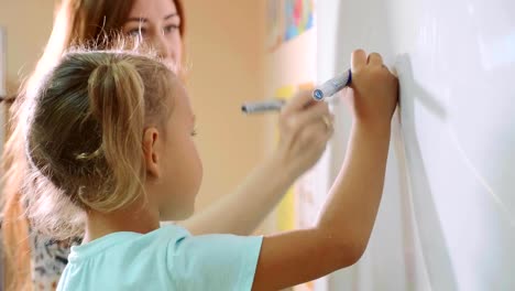 Kleine-süße-Mädchen-mit-Lehrer-schreibt-an-die-Tafel-im-Klassenzimmer