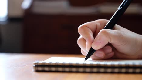 Lenta-de-la-mano-de-una-mujer-escribiendo-en-cuadernos-en-blanco-en-la-mesa-de-madera
