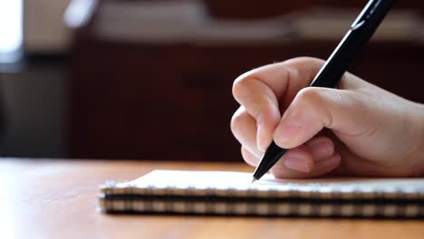 Slow-motion-of-a-woman's-hand-writing-on-blank-notebooks-on-wooden-table