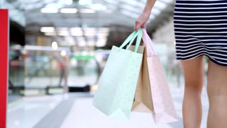 Sección-baja-de-joven-irreconocible-en-vestido-rayas-caminando-hacia-la-escalera-mecánica-con-bolsas-en-la-mano-después-de-éxito-comercial-en-ventas-día