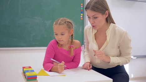 Schule-Vorbereitung,-Lehrerin-Frau-hilft-Lernenden-Mädchen-erwerben-Kenntnisse-über-Kunststoff-Figuren-am-Tisch-in-der-Nähe-Tafel-im-Klassenzimmer-der-Schule