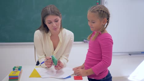 Erziehung-der-Kinder,-junge-Lehrer-mit-Kunststoff-Figuren-für-intelligente-Schülerin-am-Tisch-in-der-Nähe-von-Board-im-Klassenzimmer-der-Schule-unterrichten