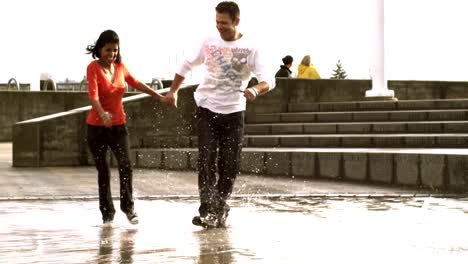 A-couple-runs-and-jumps-through-the-puddles-of-a-fountain-in-a-park