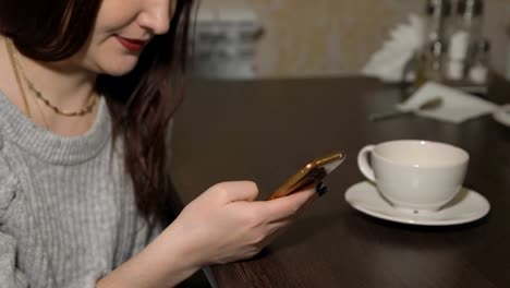 Young-woman-sitting-in-cafe-with-phone-and-drinking-tea