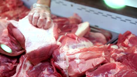 Refrigerator-in-the-store.-A-pile-of-raw-pork-meat.-Hand-butcher-turns-over-pieces-of-meat