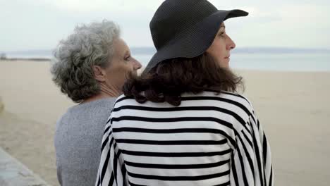 Adult-daughter-hugging-elderly-mother-and-looking-at-sea