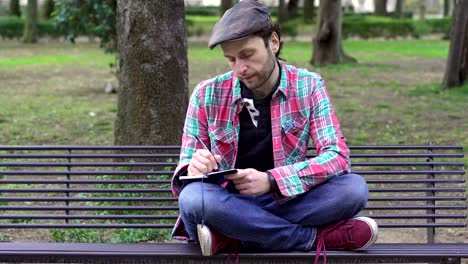 depressed-man-on-a-bench-at-the-park-writes-her-thoughts-in-a-diary