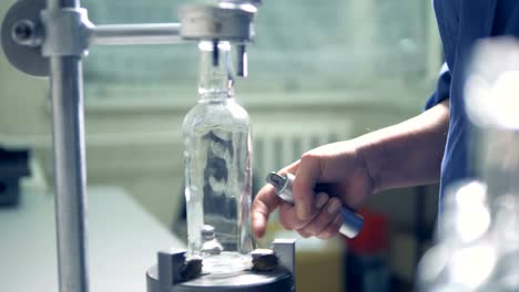 Factory-worker-checks-bottle,-rotating-it-on-a-special-instrument.-4K.