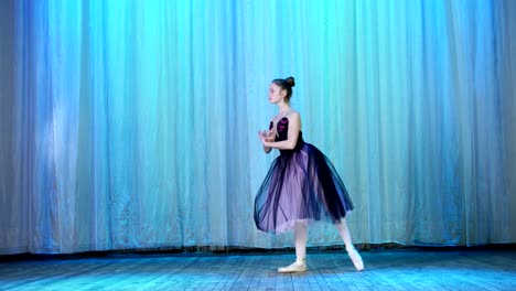 ballet-rehearsal,-on-the-stage-of-the-old-theater-hall.-Young-ballerina-in-lilac-black-dress-and-pointe-shoes,-dances-elegantly-certain-ballet-motion,-raises-her-leg-up-behind