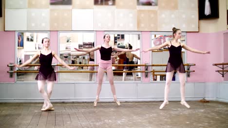 in-dancing-hall,-Young-ballerinas-in-black-leotards-perform-pas-echappe,-standing-on-toes-in-pointe-shoes-near-barre-at-mirror-in-ballet-class