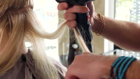 Male-hairdresser-combing-hair-to-blonde-girl-in-beauty-salon,-close-up