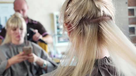 Male-hairdresser-combing-hair-to-blonde-girl-in-beauty-salon,-close-up