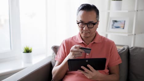 Mann-mit-TabletPC-und-Kreditkarte-zu-Hause-auf-sofa