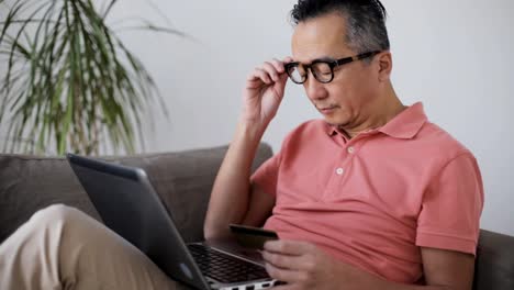 man-with-laptop-and-credit-card-on-sofa-at-home