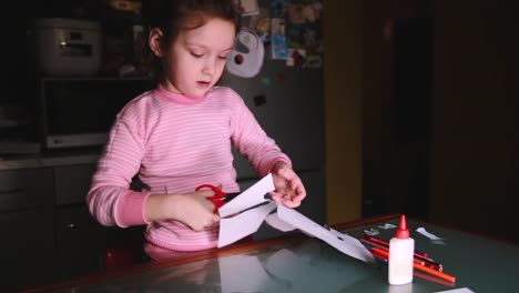 Hermosa-mujer-preescolar-europeo-niño-suéter-rosa-sentado-en-la-mesa-en-casa-formas-de-papel-de-corte