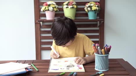 Children-homework.-Young-mixed-race-boy-doing-homework-in-terrace-at-home.-Drawing-and-writing.-Focus-mood.-Back-to-school-concept.