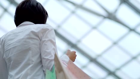 Beautiful-young-woman-looking-around-shopping-mall-while-moving-up-on-escalator-with-bunch-of-shopping-bags-in-her-hand,-slow-motion-shot