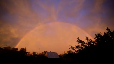 Regenbogen-am-bewölkten-Himmel-über-Stadtbild-am-Abend-bei-Sonnenuntergang.