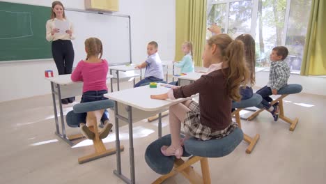Schulstunde,-führt-junge-Lehrerin-in-der-Nähe-von-Board-kognitive-Lektion-für-intelligente-Kinder-am-Schreibtisch-im-Klassenzimmer-der-Schule