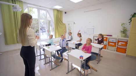 group-of-learners-raise-hands-to-answer-at-lesson-while-sitting-at-desk-in-front-of-teacher-to-blackboard-in-School-class