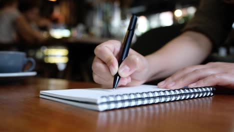 Mano-de-una-mujer-escribiendo-en-cuadernos-en-blanco-de-madera-mesa-de-café