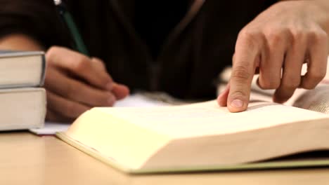 Close-up-of-a-student-taking-notes-while-reading-a-text-book