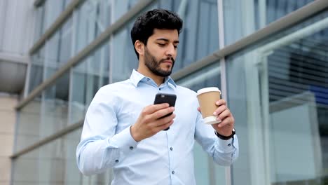 Hombre-de-negocios-guapo-con-teléfono-y-café-en-la-calle