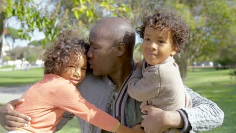 African-American-father-hugging-and-kissing-curly-children-in-park