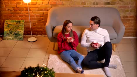 Top-down-view-of-two-young-friends-sitting-on-carpet-and-drinking-hot-beverages-communicating-in-christmas-atmosphere.