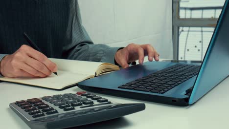 A-man-looks-into-a-laptop-and-takes-notes-in-his-notebook