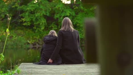 Frau-und-ihre-Tochter-sitzen-in-der-Nähe-des-Teiches.