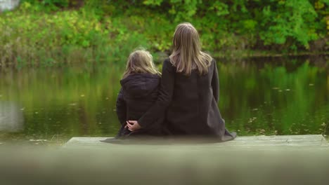 Frau-und-ihre-Tochter-sitzen-in-der-Nähe-des-Teiches.