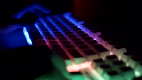 Jugador-masculino-escribiendo-y-presionando-teclas-en-el-teclado-RGB-de-juego-blanco-en-la-habitación-oscura