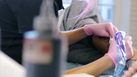 Female-tattoo-artist-with-pink-hair-making-tattoo-in-studio