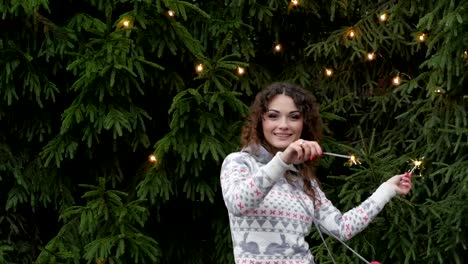 young-woman-on-the-background-of-the-Christmas-tree-and-garlands-with-sparklers.fun-and-jumps