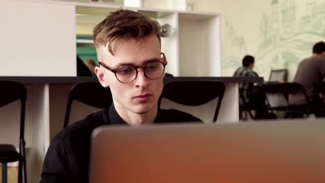 Young-male-student-in-glasses-using-laptop-in-university