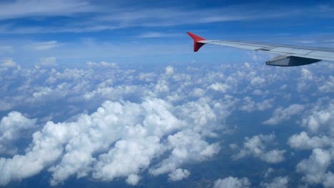 4K-footage.-traveling-by-air.-aerial-view-through-an-airplane-window.-wing-airplane-and-beautiful-white-clouds-in-blue-sky-for-background