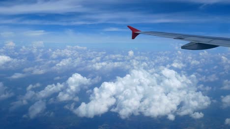 4K-footage.-traveling-by-air.-aerial-view-through-an-airplane-window.-wing-airplane-and-beautiful-white-clouds-in-blue-sky-for-background