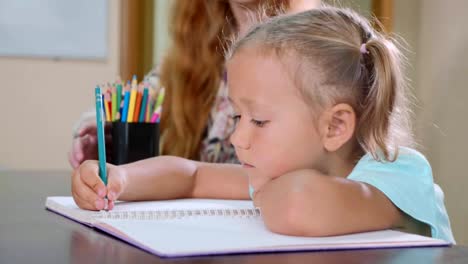 Kleine-süße-Mädchen-sitzt-im-Klassenzimmer-und-im-Heft-zu-schreiben