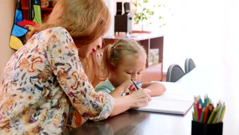 Little-cute-girl-sits-in-classroom-and-studies-with-teacher-in-exercise-book