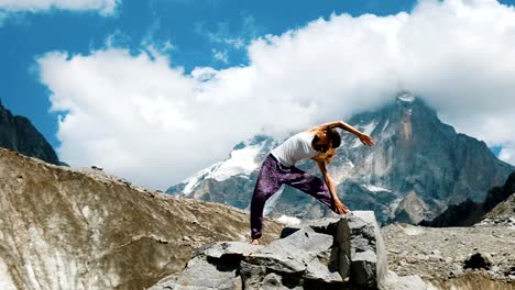 Mujer-se-dedica-a-la-gimnasia-yoga-sobre-fondo-de-una-montaña-de-nieve-en-una-excursión.-Chica-haciendo-estiramientos-al-aire-libre-en-una-caminata-al-aire-libre,-cámara-lenta