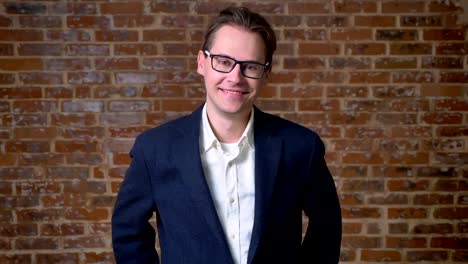 Awesome-caucasian-man-in-dark-blue-suit-and-glasses-standing-still-and-looking-straight-at-camera-in-red-studio-isolated