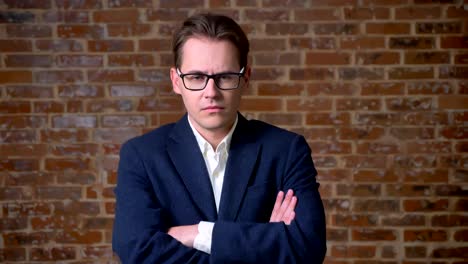 Serious-caucasian-man-in-business-suit-and-glasses-standing-and-looking-at-camera-focused-in-red-brick-studio-isolated