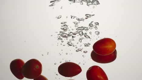 SLOW-MOTION:-Cherry-tomatoes-fall-under-water-on-white-background