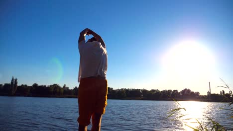 Sporty-man-standing-at-yoga-pose-on-the-edge-of-wooden-jetty-at-lake.-Young-athlete-doing-stretch-exercise-at-nature-on-sunny-summer-day.-Concept-of-healthy-active-lifestyle.-Slow-motion-Close-up