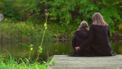 Woman-and-her-daughter-sitting-near-the-pond.