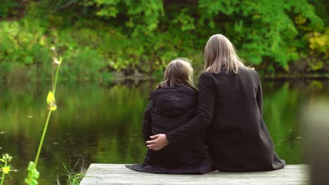 Frau-und-ihre-Tochter-sitzen-in-der-Nähe-des-Teiches.