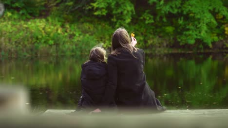 Frau-und-ihre-Tochter-sitzen-in-der-Nähe-des-Teiches.