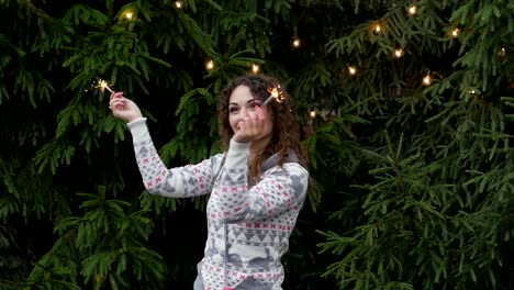 young-woman-on-the-background-of-the-Christmas-tree-and-garlands-with-sparklers.fun-and-jumps